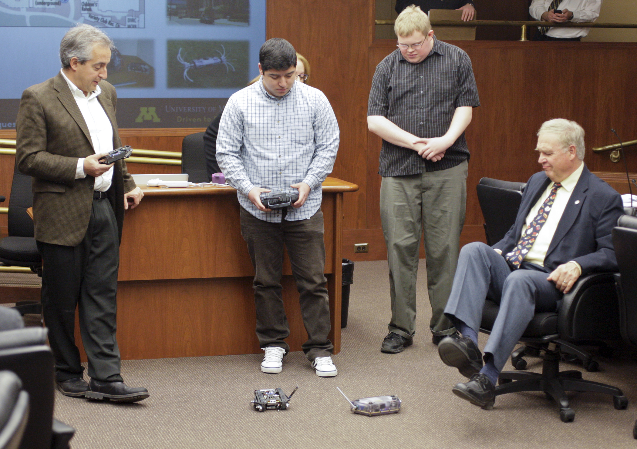 Rep. Dean Urdahl, seated, makes way for a robot being demonstrated by University of Minnesota robotics graduate student Dario Canelon during a Jan. 22 overview of the university’s bonding request before the House Capital Investment Committee. Also pictured are Dr. Nikos Papanikolopoulos, left, director of the university’s Center for Distributed Robotics, and Joshua Fasching, also a robotics graduate student. Photo by Paul Battaglia