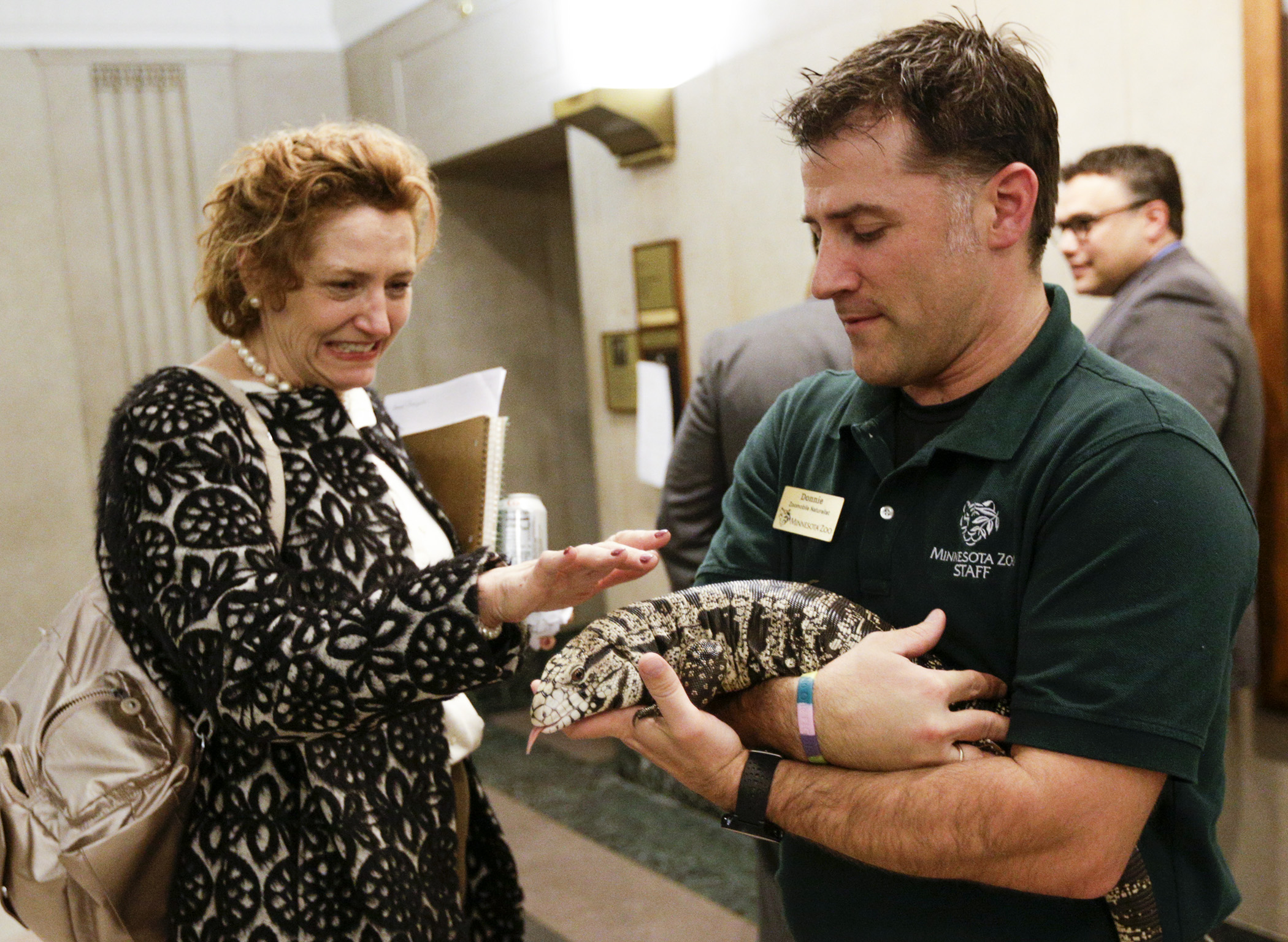 Lobbyist Sonnie Elliott reluctantly pets Evita, an Argentine black and white Tegu lizard held by Minnesota Zoo staffer Donnie Crook, before zoo leaders presented their 2018 bonding request to the House Capital Investment Committee. Photo by Paul Battaglia