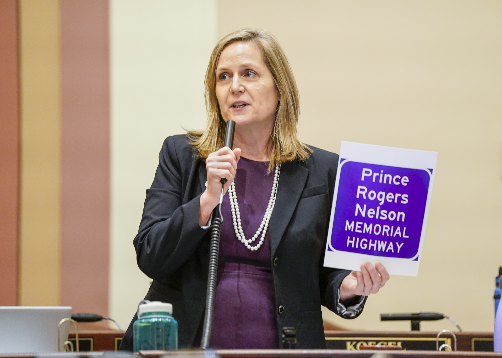 Holding up a copy of the proposed sign design, and wearing an apt color, Rep. Lucy Rehm discusses HF717, a bill to rename a segment of Highway 5 as “Prince Rogers Nelson Memorial Highway.” The bill passed 121-0 Friday. (Photo by Catherine Davis)